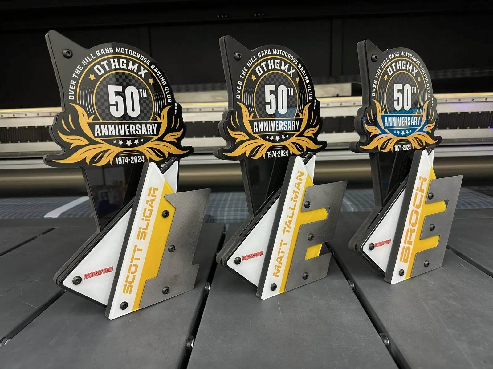 Three shaped acrylic club trophies, each with a printed anniversary graphic above an individual rider name plate