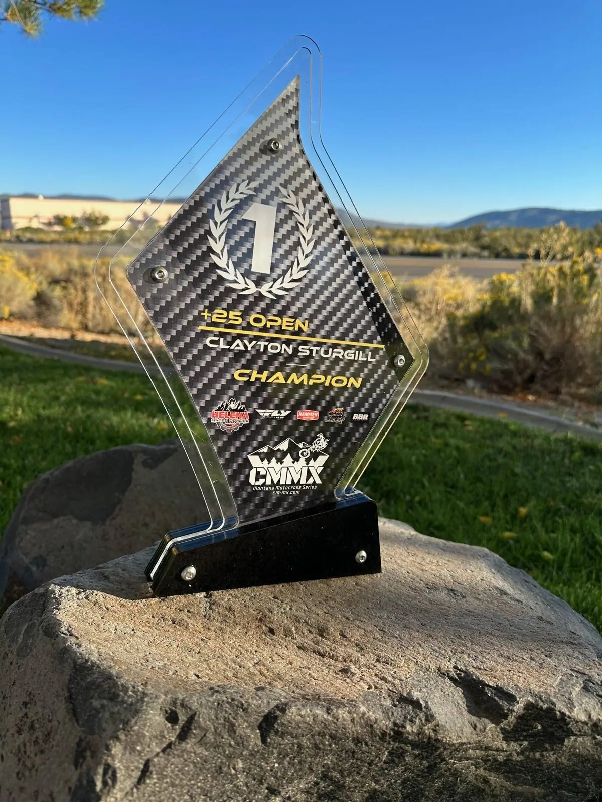 Layered acrylic champion award with a carbon-fibre-look printed panel reading 1st, +25 Open, Champion, mounted on a black base with sponsor logos