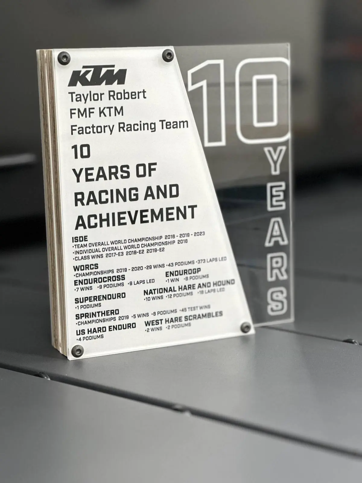 A wood-backed acrylic achievement plaque listing a rider’s off-road results season by season