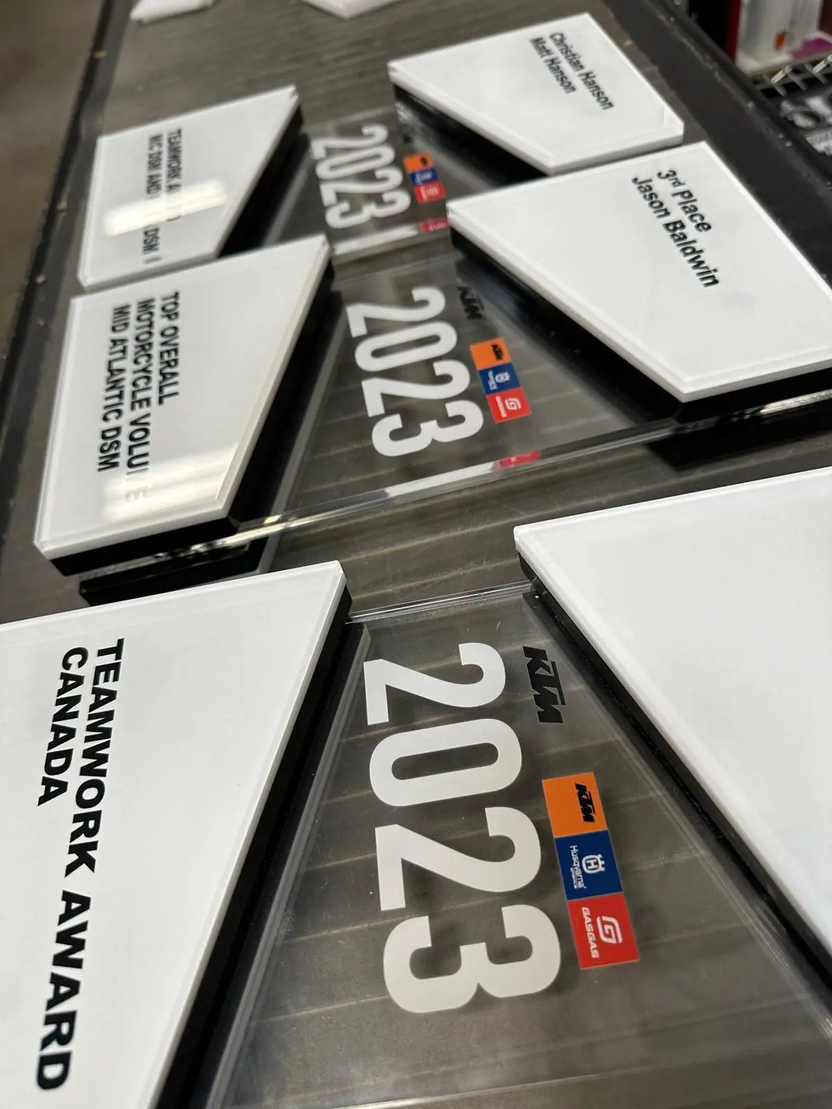A tray of white and clear acrylic plate awards laid out flat, each with a different class and placing printed on it