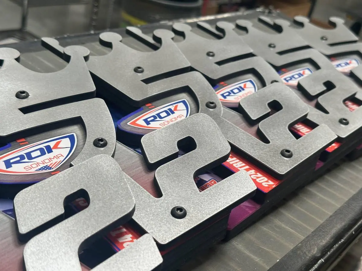 A stack of identical laser-cut numeral awards in a brushed-metal finish, produced as one batch