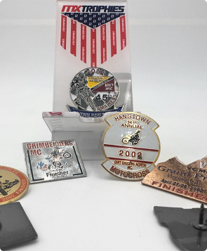 Group of custom pin awards on branded backing cards, including a Hangtown motocross event pin, a club pin and a bronze finisher pin