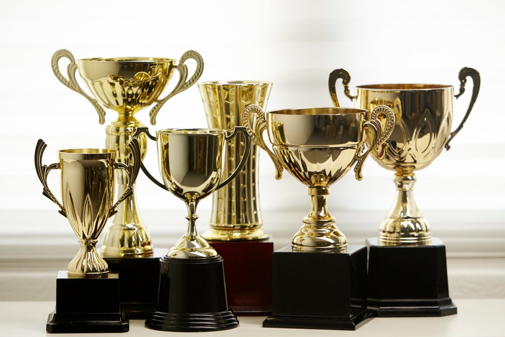 Group of gold cup trophies in assorted shapes and sizes on black bases