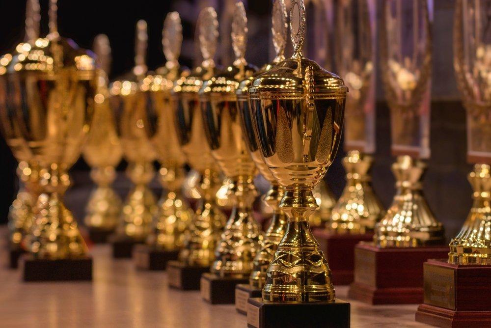 Rows of tall lidded gold trophies arranged on a table before a prize-giving
