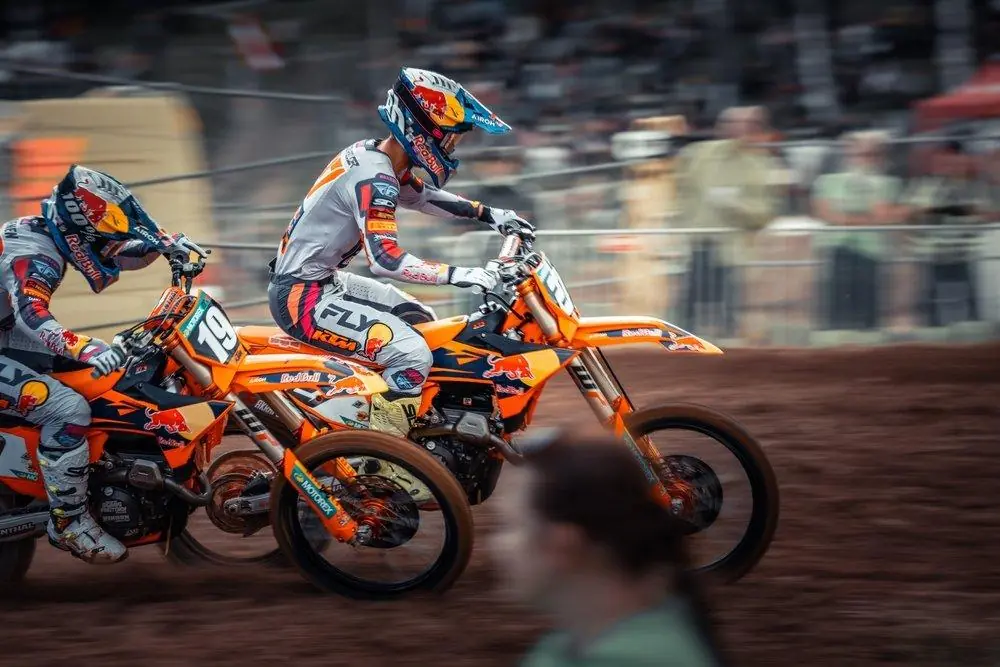 Two motocross riders on KTM bikes racing side by side through a dirt corner