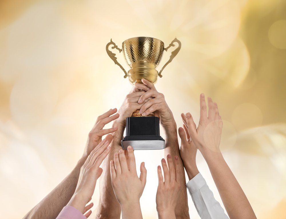 Many hands reaching up towards a gold cup trophy held aloft