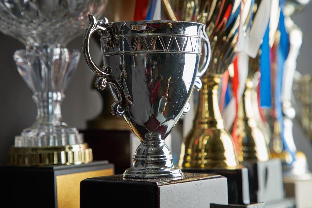 Trophy,Awards,For,Champion,Leadership Close-up of a silver cup trophy on a black base, with gold trophies and medal ribbons behind
