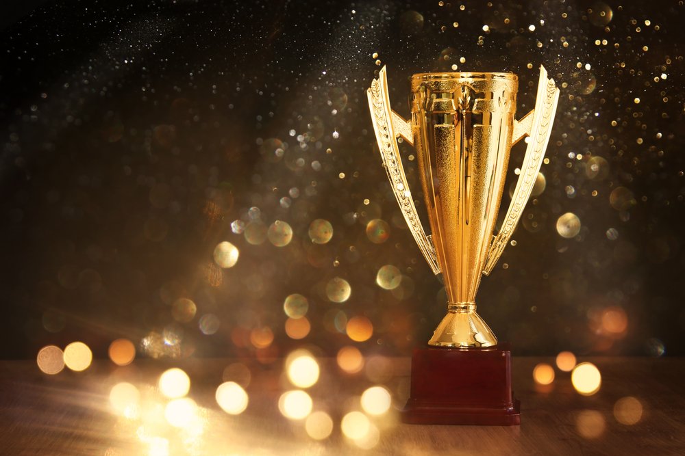 Gold cup trophy on a wooden base against a dark background scattered with golden bokeh lights