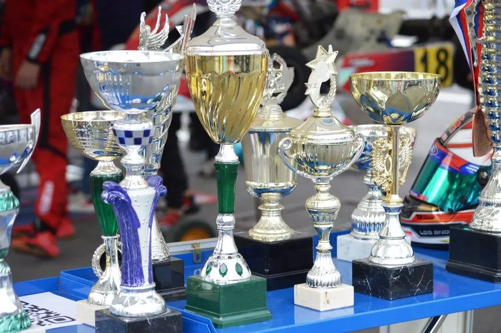 Interior,Items,For,Design,And,Relaxation Cup trophies of various sizes lined up on a blue table in a race paddock beside a helmet